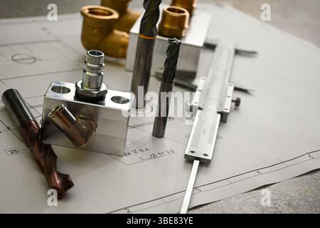 Metallbohrer, Schaftfräser, Messschieber und Klempnerverbinder, die auf einer technischen Zeichnung liegen und Präzision und Ingenieurskunst demonstrieren. Stockfoto