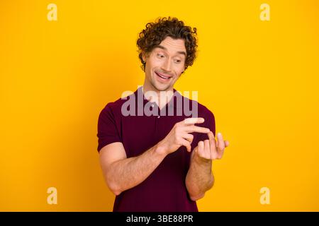 Der junge Gentleman im burgunderroten Pologesten spielt vor leuchtendem gelbem Hintergrund für einen lässigen Stil Stockfoto