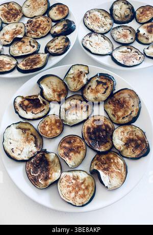 Gegrillte Auberginen-Scheiben auf weißen Tellern, isoliert auf einem weißen Tisch. Gesunde und vegetarische Lebensmittel. Direkt darüber. Stockfoto
