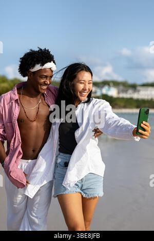 Vielfältige Paare verbunden, mit Technologie und sozialen Medien, während Sie Momente am Strand genießen Stockfoto