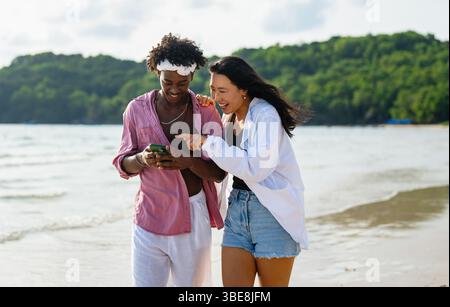 Vielfältige Paare verbunden, mit Technologie und sozialen Medien, während Sie Momente am Strand genießen Stockfoto