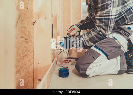 Ein gelernter Elektriker arbeitet an der Verdrahtung in einem im Bau befindlichen Wohngebäude, um Sicherheit und Funktionalität zu gewährleisten. Stockfoto