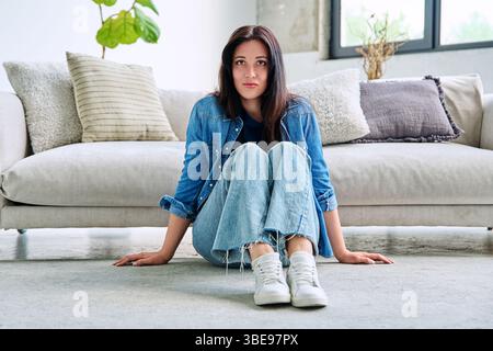 Porträt einer schönen jungen brünetten Frau, die in der Nähe des Sofas im Wohnzimmer sitzt Stockfoto