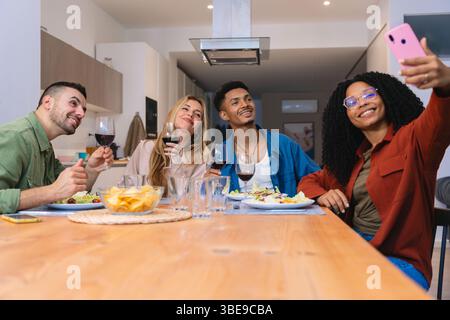 Gruppe von Freunden, die Selfie nehmen und während des Abendessens zu Hause mit Wein toasten Stockfoto