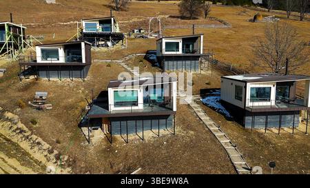 Moderne Hütten am Hang in ländlicher Landschaft. Blick aus der Vogelperspektive auf moderne Hütten mit großen Fenstern und Terrassen in einer rustikalen Landschaft Stockfoto