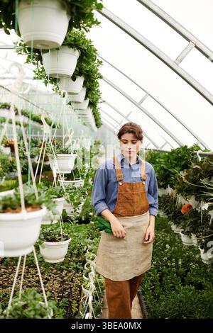 Eine junge Frau pflegt geschickt ihre Topfpflanzen in einem blühenden Gewächshaus, in dem sie sich in Glückseligkeit ergossen. Stockfoto