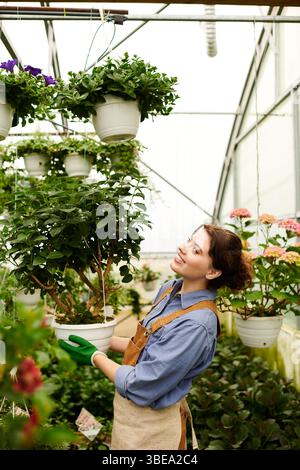Eine junge Frau pflegt gekonnt Pflanzen in einem lebendigen Gewächshaus, umgeben von Grün. Stockfoto