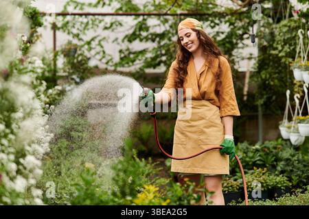 Eine junge Frau mit Kopftuch tränkt ihre Pflanzen in einem lebendigen Gewächshaus. Stockfoto