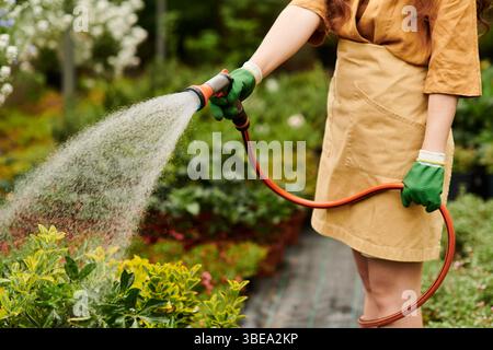 Entzückte Gärtnerin im Kopftuch Wasser üppige Pflanzen in ihrem blühenden Gewächshaus. Stockfoto