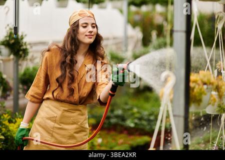 In einem lebendigen Gewächshaus neigt eine junge Frau mit Kopftuch zu Pflanzen und strahlt Glück aus. Stockfoto