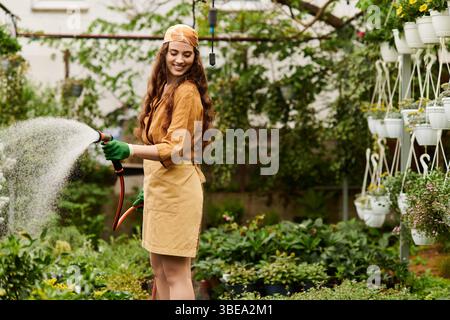 Entzückende Gärtnerin mit Kopftuch, das in einem sonnigen Gewächshaus Pflanzen pflegt. Stockfoto