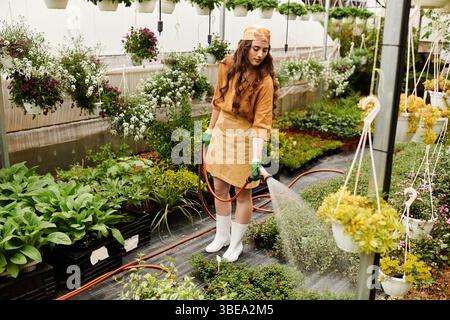 Eine glückliche Gärtnerin lebt in einem hellen Gewächshaus und zeigt ihre Liebe zur Natur. Stockfoto