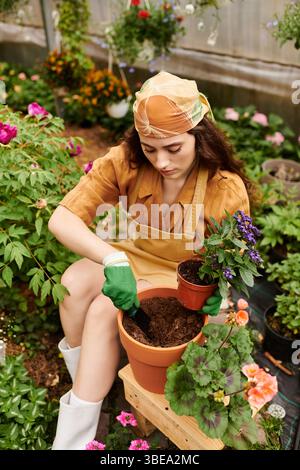 Eine junge Frau im Kopftuch pflanzt freudig in einem lebendigen Gewächshaus. Stockfoto