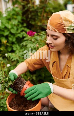Eine junge Frau mit Kopftuch pflegt liebevoll ihre Pflanzen in einem lebendigen Gewächshaus. Stockfoto