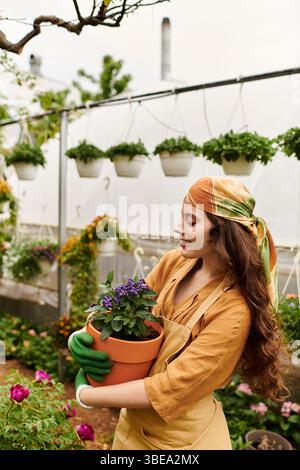 Frau mit Kopftuch und Schürze pflanzt in einem lebendigen Gewächshaus. Stockfoto