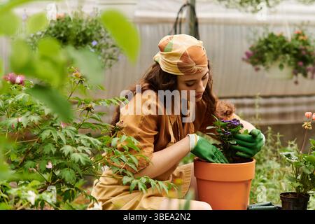 Der begeisterte junge Gärtner im Kopftuch tendiert zu bunten Pflanzen in einem hellen Gewächshaus. Stockfoto
