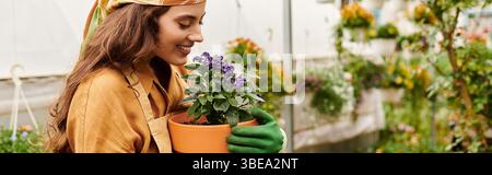 Eine junge Frau im Kopftuch pflegt liebevoll ihre Pflanzen, umgeben von üppigem Grün, Banner Stockfoto