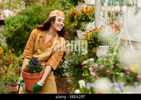 Eine junge Frau im Kopftuch lächelt fröhlich, während sie sich um Pflanzen in einem üppigen Gewächshaus kümmert. Stockfoto