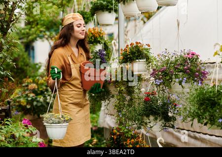 Eine glückliche junge Frau mit Kopftuch und Schürze tendiert dazu, in einem Gewächshaus Pflanzen zu blühen. Stockfoto