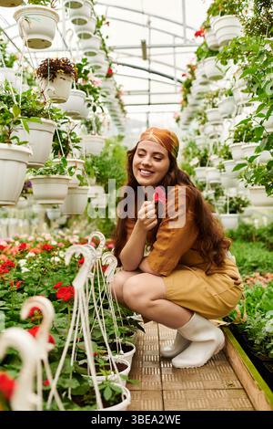 Eine glückselige Frau in einem Kopftuch neigt zu lebendigen Pflanzen, die die Schönheit der Natur in einem Gewächshaus umschmeicheln. Stockfoto