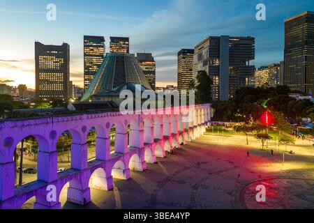 Lapa Aquädukt, beleuchtet mit violetten und rosa Farben am Abend mit hohen Bürogebäuden in der Innenstadt von Rio de Janeiro Stockfoto