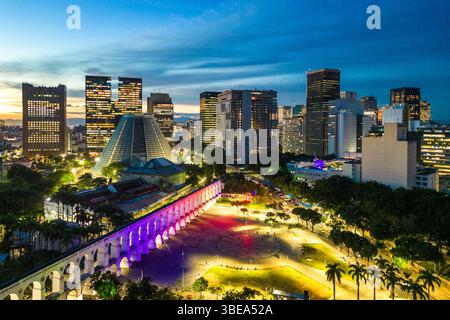 Lapa Aquädukt, beleuchtet mit violetten und rosa Farben am Abend mit hohen Bürogebäuden in der Innenstadt von Rio de Janeiro Stockfoto