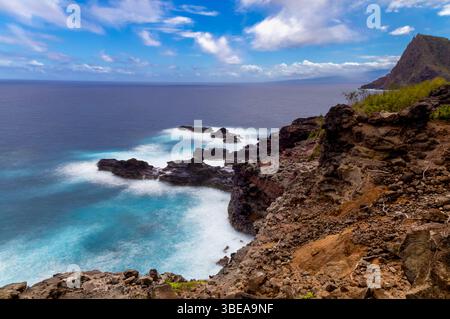 Maui, Hawaii, USA - 9. April 2022: Wellen krachen gegen die felsige Küste von Maui und schaffen einen schönen Kontrast zwischen blauem Wasser und Dunkelheit Stockfoto