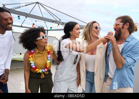 Freunde singen Karaoke auf einer Dachparty und genießen gemeinsam den Sommer Stockfoto