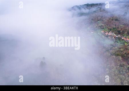 Verstecktes Dorf, das durch dichte Nebelbank auftaucht, Hochwinkelansicht, Drohnenbild Stockfoto