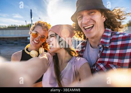 Drei fröhliche junge Freunde machen ein Selfie im Freien, genießen die Sonne und genießen gemeinsam einen lebhaften Tag in der Stadt Stockfoto