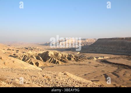 Riesige Wüstenlandschaft in der Negev-Region im Süden Israels mit dramatischen Erosionsmustern, zerklüfteten Hügeln und klarem blauen Himmel darüber. Stockfoto