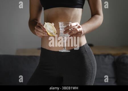 Nahaufnahme einer jungen schlanken Frau, die Wasser mit Zitronensaft zubereitete. Morgendliches Ritual. Gesundes Antioxidans. Schlankheitsdiät. Stärkung der Immunität und des Stoffwechsels. Stockfoto