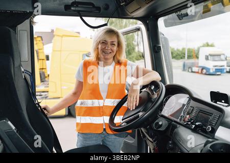 Reife Frau LKW-Fahrer Lenkrad in der LKW-Kabine. Glückliches Mittelalter-Lkw-Porträt. Stockfoto