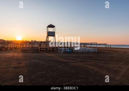Wunderschöne Sonnenaufgangsszene an einem leeren Strand mit einem Rettungsschirmturm und angeordneten Holzunterkünften, die Ruhe und Gelassenheit hervorrufen. Kaspisches Meer, Buz Stockfoto