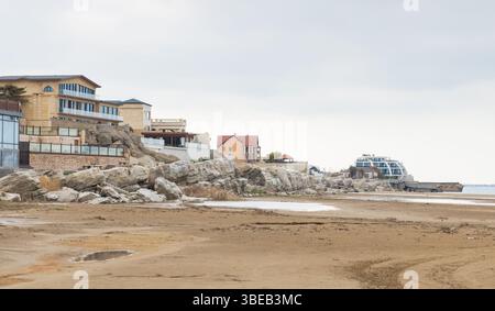 Buzowna, Aserbaidschan. Foto der Küstenlandschaft mit Häusern in der Nähe eines Sandstrandes und einer felsigen Küste, unter einem ruhigen, bewölkten Himmel, der an einen erinnert Stockfoto