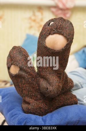 Wollsocken mit riesigen Löchern auf die Beine eines Mannes Stockfoto