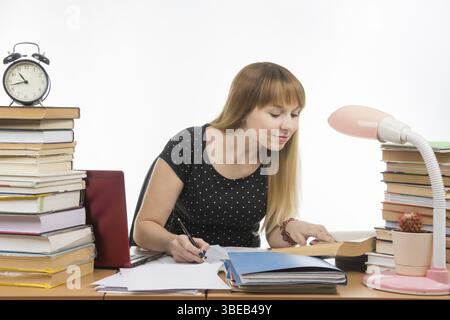 Hübschen weiblichen Schüler an einem Tisch mit Büchern in der Bibliothek schreiben Job übersät Stockfoto