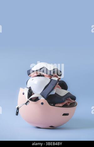Draufsicht der Schutzausrüstung für Rollschuhe – Knie-, Ellenbogen- und Handgelenkpolster und Helm in rosa Farben. Blauer Hintergrund, flache Lagen. Stockfoto