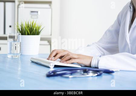 Arzt, der an der Computertastatur tippt. Arzt in der medizinischen Uniform arbeitet mit Computer am Schreibtisch im Büro. Moderne Technik in der Untersuchung und Diagnose Stockfoto