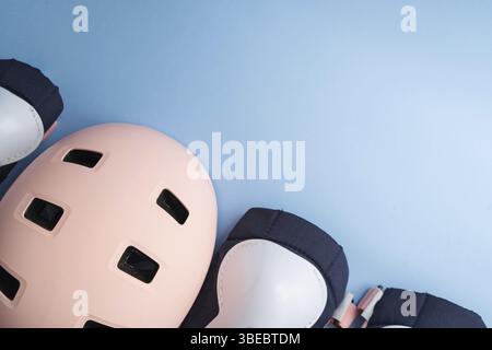 Draufsicht der Schutzausrüstung für Rollschuhe – Knie-, Ellenbogen- und Handgelenkpolster und Helm in rosa Farben. Blauer Hintergrund, flache Lagen. Stockfoto