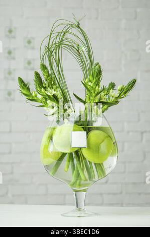 Eine vertikale Aufnahme von Ornithogalum und Äpfeln in einer großen Glasschale auf einem Tisch Stockfoto