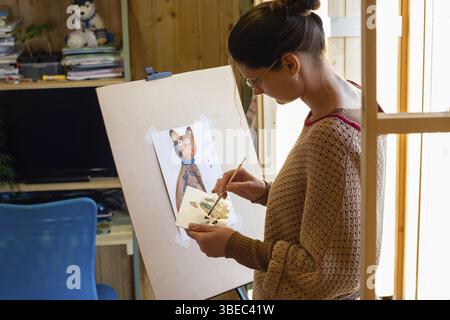 Der Künstler mischt zu Hause Farben auf einem Palettengemälde Am Fenster Stockfoto