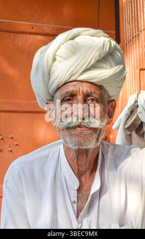Älterer Mann mit traditionellem Rajasthani Turban lächelnd glücklich in die Kamera mit warmen Orangetönen im Hintergrund Stockfoto