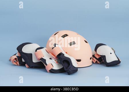 Draufsicht der Schutzausrüstung für Rollschuhe – Knie-, Ellenbogen- und Handgelenkpolster und Helm in rosa Farben. Blauer Hintergrund, flache Lagen. Stockfoto