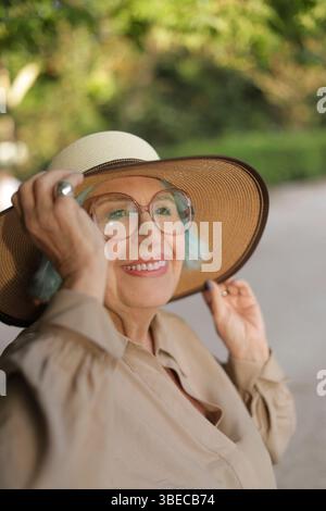 Ältere Frau mit Hut lächelt zur goldenen Stunde Stockfoto