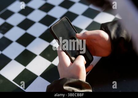 Die Hände eines jungen Mannes halten das Handy auf dem Schachbrett Stockfoto
