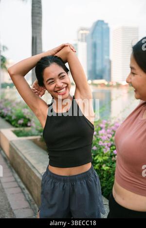 Zwei fröhliche Athleten, die sich in einem pulsierenden Stadtpark von bangkok ausstrecken und die Vorteile der Fitness und der Schönheit der urbanen Natur unter genießen Stockfoto