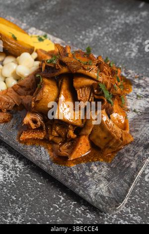 Köstlicher, würziger Mondongo, serviert auf einem rustikalen Teller, begleitet von gekochten Kartoffeln mit huancaína-Sauce und Chocolo-Mais, einem traditionellen peruanischen Gericht Stockfoto