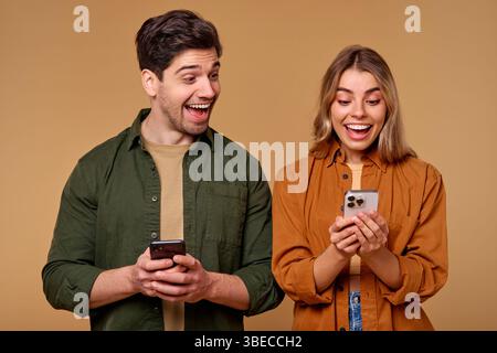 Ein fröhliches junges Paar, voller Glück, interagiert mit ihren Smartphones auf eine reizvolle und spielerische Art und Weise und zeigt ihre Aufregung lebhaft Stockfoto