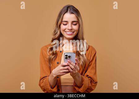 In einer warmen Atmosphäre strahlt eine fröhliche und Jugendliche junge Frau vor Glück, während sie mit ihrem Smartphone in Berührung kommt und die ess perfekt hervorhebt Stockfoto